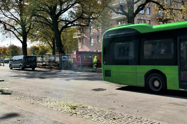 Image of a city street with a bus, a house being built in the background and a pave way for bikes and pedestrians